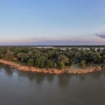 A panoramic view of a river meeting a lush, forested landmass at sunset.