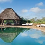 Ein ruhiger Swimmingpool mit einer Strohhütte und Liegesitzen daneben, in einer sonnigen Außenterrasse.