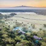 Aerial view of Solio Lodge surrounded by lush greenery with a distant mountain in the background at sunrise.