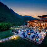 Ein luxuriöser Gästebereich mit Sitzgelegenheiten im Freien und dekorativen Laternen bei Dämmerung, mit Blick auf grüne Hügel und Berge in Bhutan.