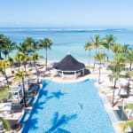 A luxurious swimming pool surrounded by palm trees at a tropical resort overlooking the ocean.