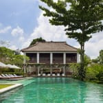 Ein luxuriöser Außenpool vor einem traditionell gestalteten Gebäude, umgeben von üppigem Grün in Bali.