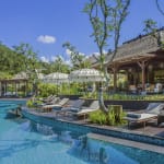 Luxurious outdoor pool area at Mandapa, a Ritz-Carlton Reserve, with lounge chairs, umbrellas, and shaded seating under trees.