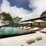 Ein luxuriöser Poolbereich im Kura Boutique Hotel in Uvita, Costa Rica, mit Sonnenliegen und Sonnenschirmen, die auf grüne Bäume und Berge blicken.