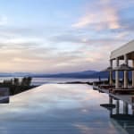 Ein Infinity-Pool mit Blick auf das Meer bei Sonnenuntergang, mit Sonnenschirmen und Liegestühlen in der Nähe.