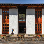 A woman walks past a traditional Bhutanese building with white walls and wooden windows.