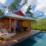 Eine hölzerne Lodge mit einem kleinen Pool in einer grünen, bergigen Landschaft, mit einem Outdoor-Sitzbereich und Liegestühlen.