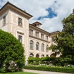 Elegant multi-story hotel building with classic architecture, surrounded by lush green trees and a well-maintained garden.