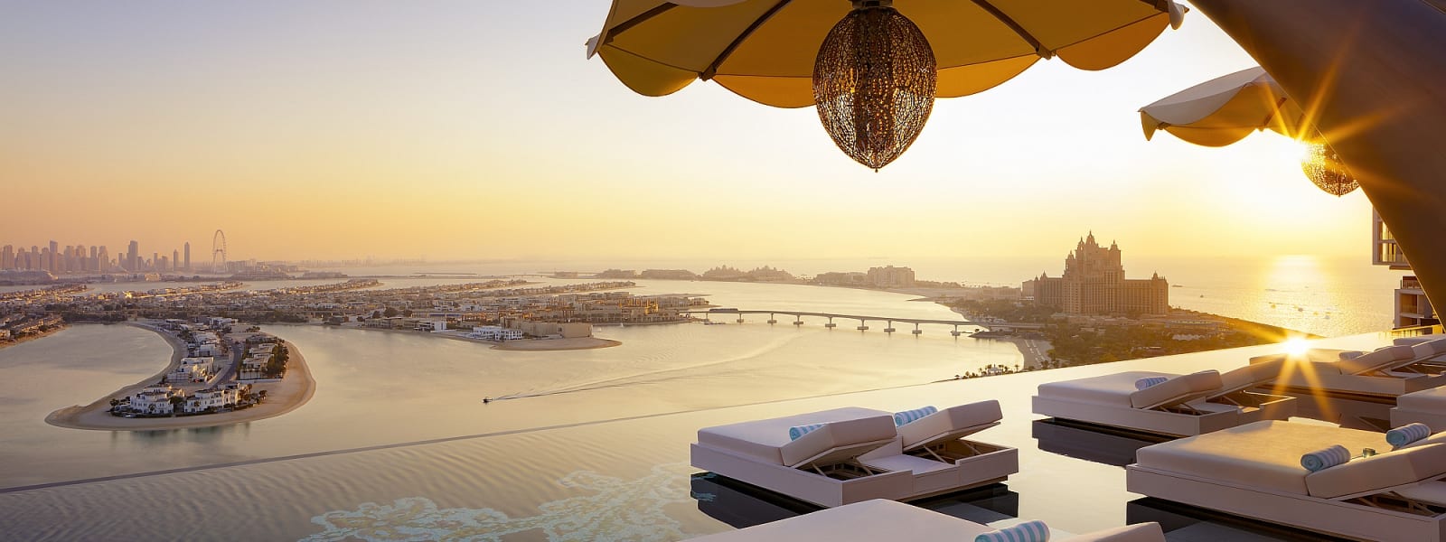 Luxuriöse Outdoor-Poolarea mit Liegen und Sonnenschirmen, Blick auf Fluss und Stadt bei Sonnenuntergang.