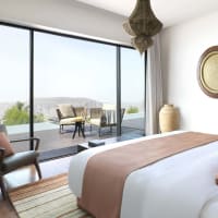 Ein luxuriöses Schlafzimmer mit großem Bett, Sitzbereich und Balkon mit Outdoor-Stühlen und Blick auf die Hügel.