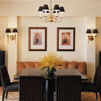 Eleganter Speisesaal mit einem schwarzen rechteckigen Tisch, sechs gestreiften Stühlen, einer beige gepolsterten Bank mit Kissen, einem Kronleuchter und Wandkunst.