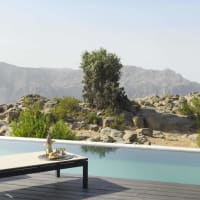 Luxuriöse Poolterrasse mit Blick auf eine felsige Wüstenlandschaft mit verstreuten grünen Sträuchern und Bergen im Hintergrund.