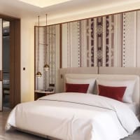 Ein luxuriöses Hotelzimmer mit einem großen Bett, weißen Bettwäsche und dekorativen Kissen, mit einer gemusterten Wand hinter dem Kopfteil und modernen Hängeleuchten.