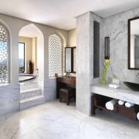 Luxuriöses Hauptbadezimmer mit Marmorflächen, dekorativen Bögen, einer Badewanne am Fenster und einer Waschtisch mit zwei Spiegeln.