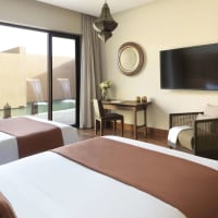 Zwei Einzelbetten in einem modernen Hotelzimmer mit einer Schiebetür, die zum privaten Garten und Pool führt.