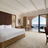 Luxuriöses Hotelzimmer mit großem Bett, Sitzecke und Balkon mit Meerblick.