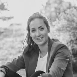 A young woman sitting outdoors with trees in the background, smiling at the camera.