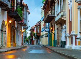 Empty historic street in Cartagena at dusk with colorful colonial buildings and lit street lamps reflecting on wet pavement.
