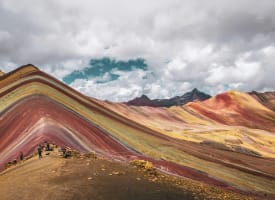 Bunte Regenbogenberge in Peru mit lebhaften Streifen in Rot, Gelb und Grün unter bewölktem Himmel.