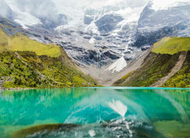 Türkisfarbener Humantay-See, der grüne Hügel und schneebedeckte Berge in Cusco, Peru, reflektiert.