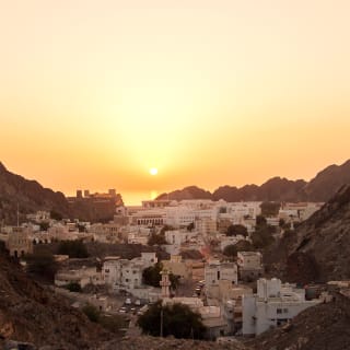 Sonnenuntergang über einer Stadt zwischen wilden Bergen in Muskat, Oman.
