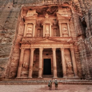 Zwei Touristen stehen vor den alten in den Felsen gehauenen Gräbern von Petra in Jordanien, kunstvoll in die Bergwand gemeißelt.