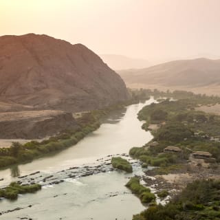 Eine malerische Wüstenlandschaft in Namibia, durchzogen von einem ruhigen Fluss, der sich durch das karge, felsige Terrain schlängelt.