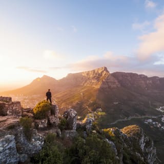 Mann steht auf einem Fels und schaut auf ein Bergpanorama