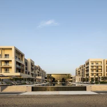 Modernes Hotelkomplex mit symmetrischen weißen Gebäuden, die eine Wasseranlage und Treppen umgeben, unter klarem blauen Himmel.