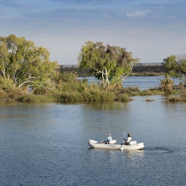 Two people paddling a kayak on the river near lush green trees and islands.
