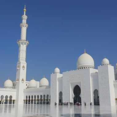 Majestic white mosque with domes and a tall minaret under a clear blue sky.