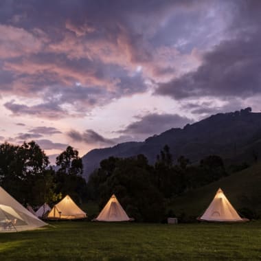 Glamorous camping tents set up on lush green grass with a mountainous backdrop at sunset.