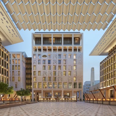 Ein moderner architektonischer Platz mit symmetrischen Gebäuden auf beiden Seiten und einem zentralen Hochhaus in Doha, Katar, mit dekorativen Dachstrukturen darüber.