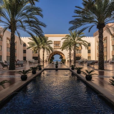 Luxurious hotel courtyard with a long water feature, surrounded by tall palm trees and seating areas.