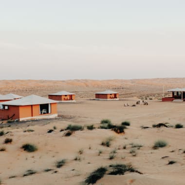 A remote desert campsite with several small orange buildings spread across sandy dunes.