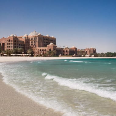 Luxuriöse Hotel- und Resortgebäude in der Nähe eines Sandstrandes mit türkisfarbenem Wasser unter klarem blauen Himmel.