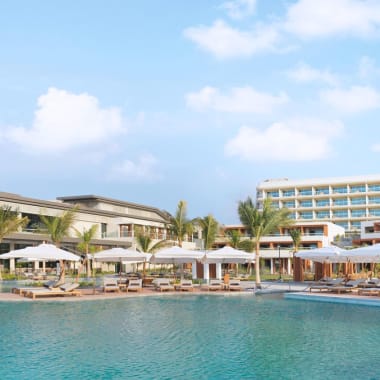 Luxushotel mit Swimmingpool, Palmen und Sonnenschirmen in Küstennähe.