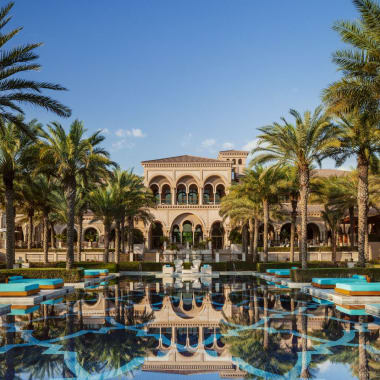 Luxuriöses Resort mit einem großen Gebäude, umgeben von Palmen und einem reflektierenden Pool im Vordergrund.