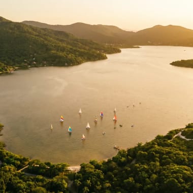 Luftaufnahme der Lagoa da Conceição in Florianópolis mit türkisem Wasser, weißen Sanddünen und Atlantikküste im goldenen Abendlicht