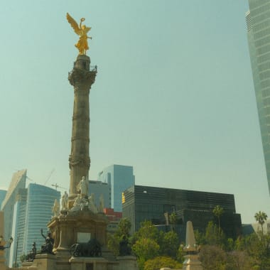 Das Unabhängigkeitsdenkmal in Mexiko-Stadt mit einer goldenen Engelsfigur auf einer hohen Säule, umgeben von modernen Wolkenkratzern und Grünflächen.