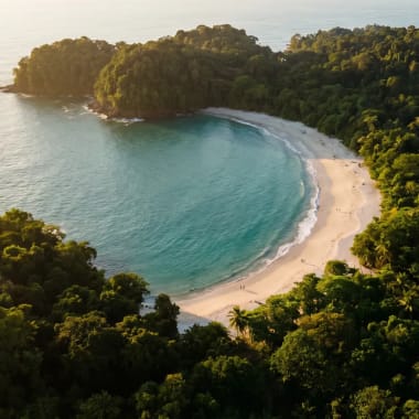 Hufeisenförmige Bucht von Playa Manuel Antonio mit türkisem Wasser und Regenwald im Morgenlicht