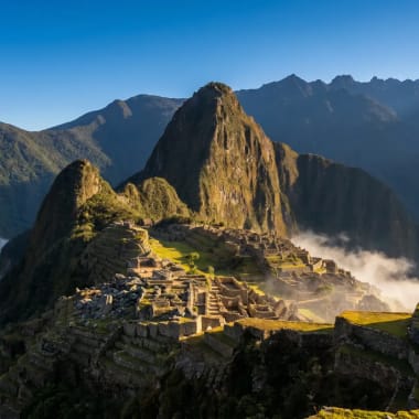Antike Inka-Ruinen von Machu Picchu im Sonnenlicht beleuchtet, umgeben von Bergen und Wolken unter der Stätte.