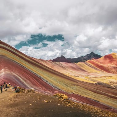 Bunte Regenbogenberge in Peru mit lebhaften Streifen in Rot, Gelb und Grün unter bewölktem Himmel.