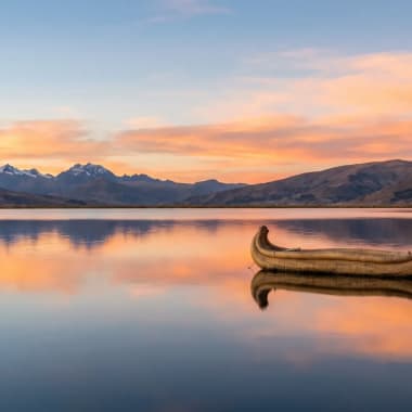 Titicacasee mit traditionellem Totora-Schilfboot im Vordergrund und schneebedeckter Andenkulisse im Hintergrund
