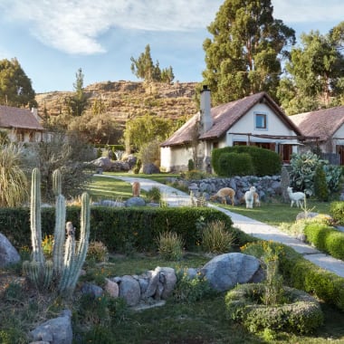 Hübsche kleine Häuser mit schrägem Dach in einem üppigen, grünen Garten bei Las Casitas, Belmond Hotel, umgeben von Bäumen und Steinen.
