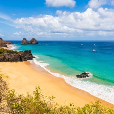 Beautiful sandy beach with turquoise waters and rocky formations, viewed from a high vantage point on a sunny day.