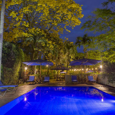 A beautifully lit outdoor swimming pool surrounded by trees and lounge chairs at night in Pereira, Colombia.