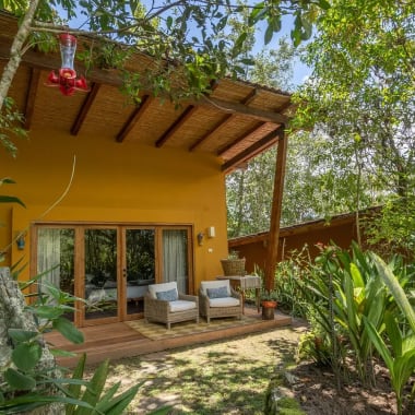 A cozy outdoor seating area in a lush garden with a yellow house in the background.