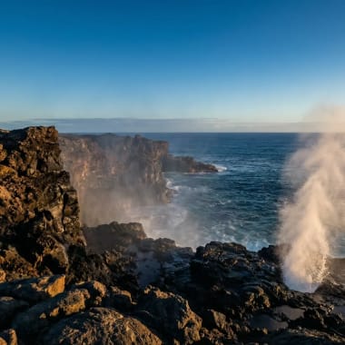 Steilklippen auf der Insel Española im Galápagos-Archipel mit Sprühfontäne des Blowholes bei Sonnenuntergang