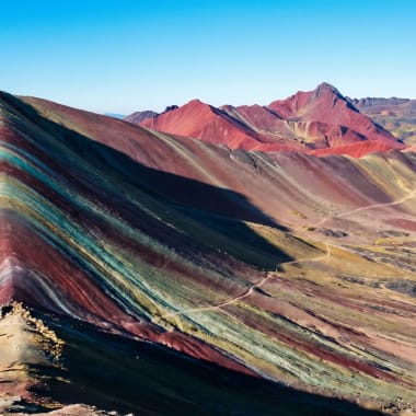 Vinicunca Rainbow Mountain in Peru mit roten, gelben und türkisen Mineralschichten im Morgenlicht vor den Anden